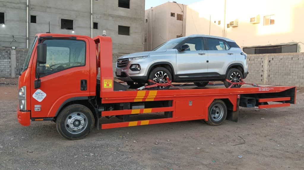 Orange flatbed tow truck carrying silver SUV